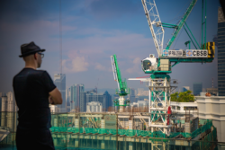 都市の高層ビル群を背景に、建設現場の大型クレーンを眺める人物が写った風景写真
